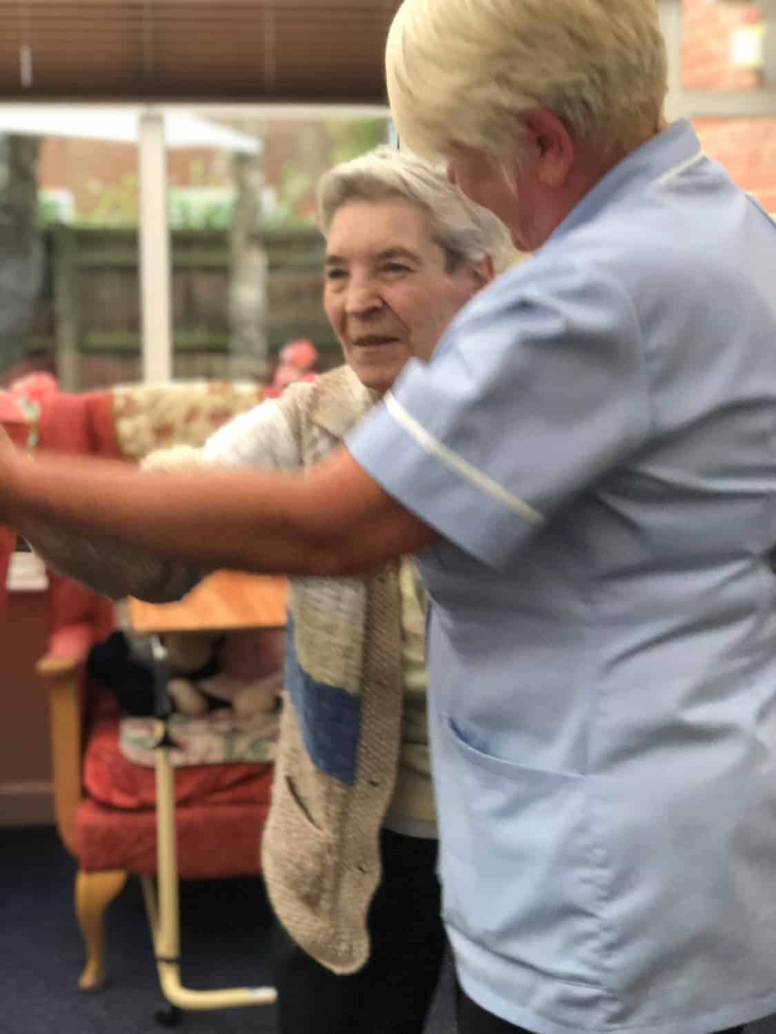 A caregiver gently assists an elderly woman through an art gallery, providing support and guidance with a warm touch.
