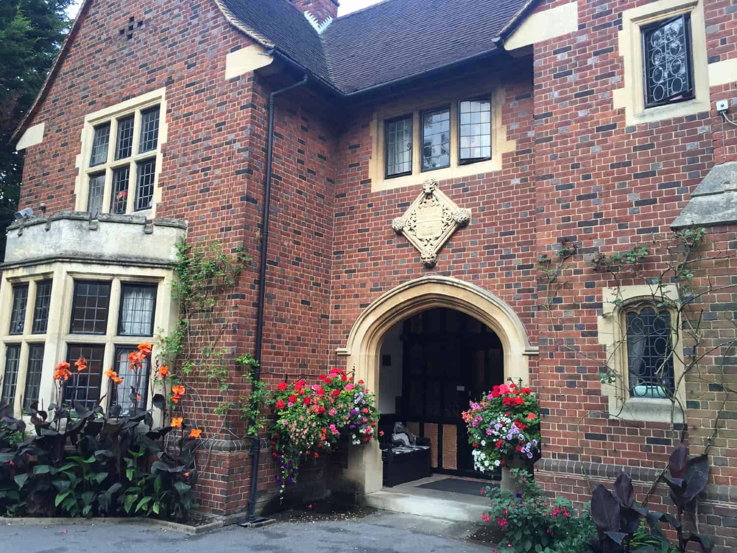 An inviting family-run brick house with an arched entryway, adorned with vibrant flower pots and climbing greenery that adds charm to the traditional architecture.