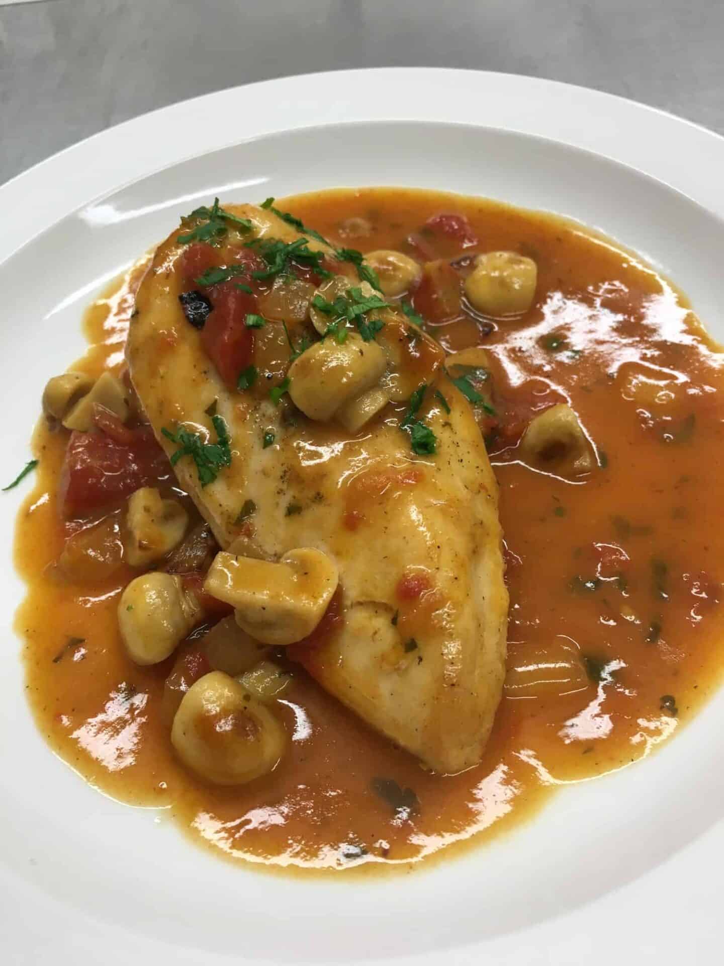 A plate of homemade chicken breast simmered in a rich tomato sauce with mushrooms and herbs, garnished with chopped parsley.
