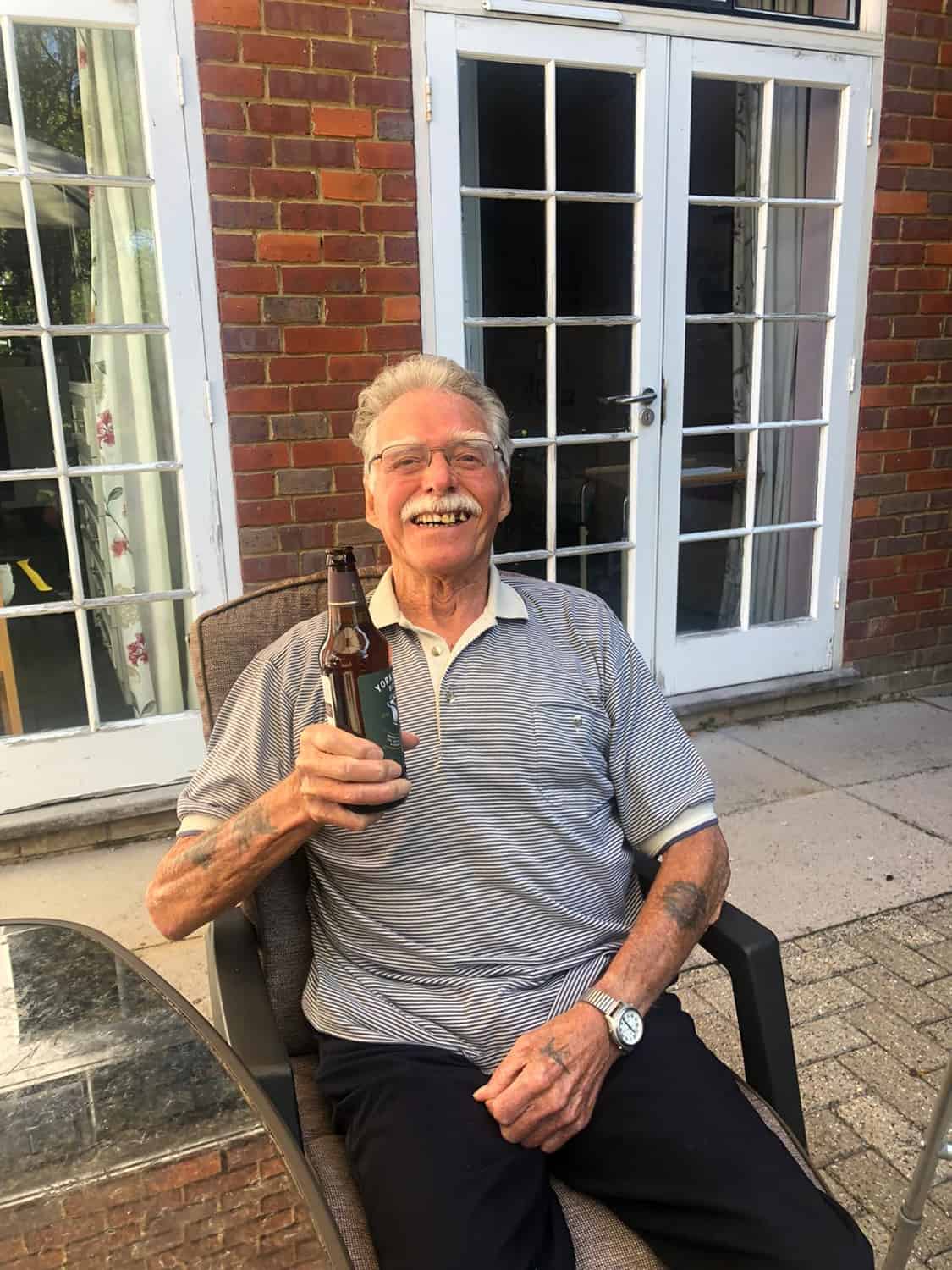 A smiling person relaxing outdoors with a bottle in hand, enjoying a beautiful day at an art exhibition.