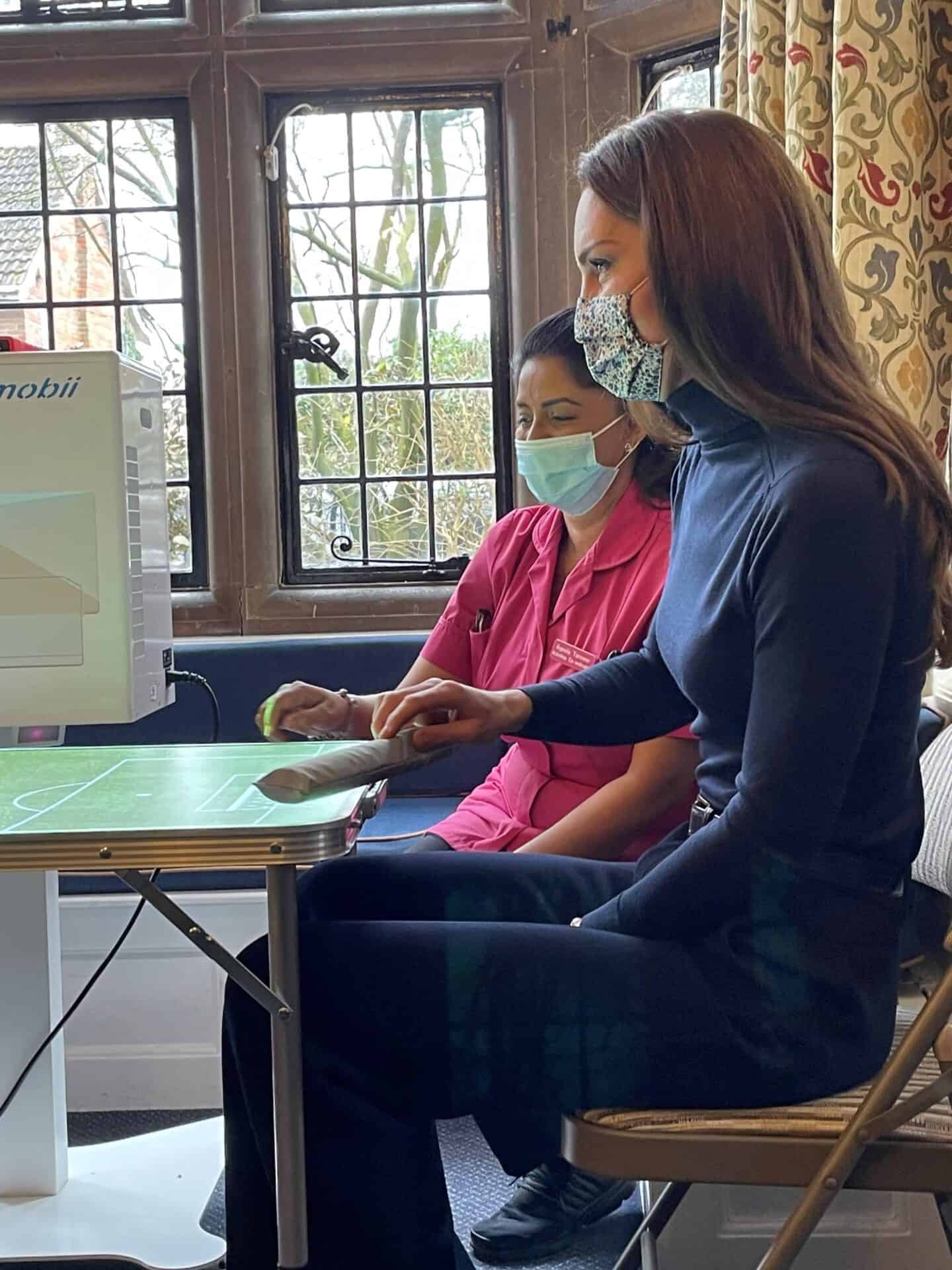 The Princess of Wales sits next to a resident at the Oxford House Nursing Home; focused on an interactive feature, a tabletop activity in a room with traditional decor.