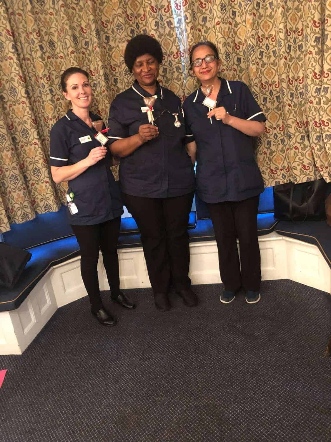 Three healthcare professionals in uniform standing together with smiles in a gallery, each holding a syringe, likely representing their role in patient care or a vaccination campaign.