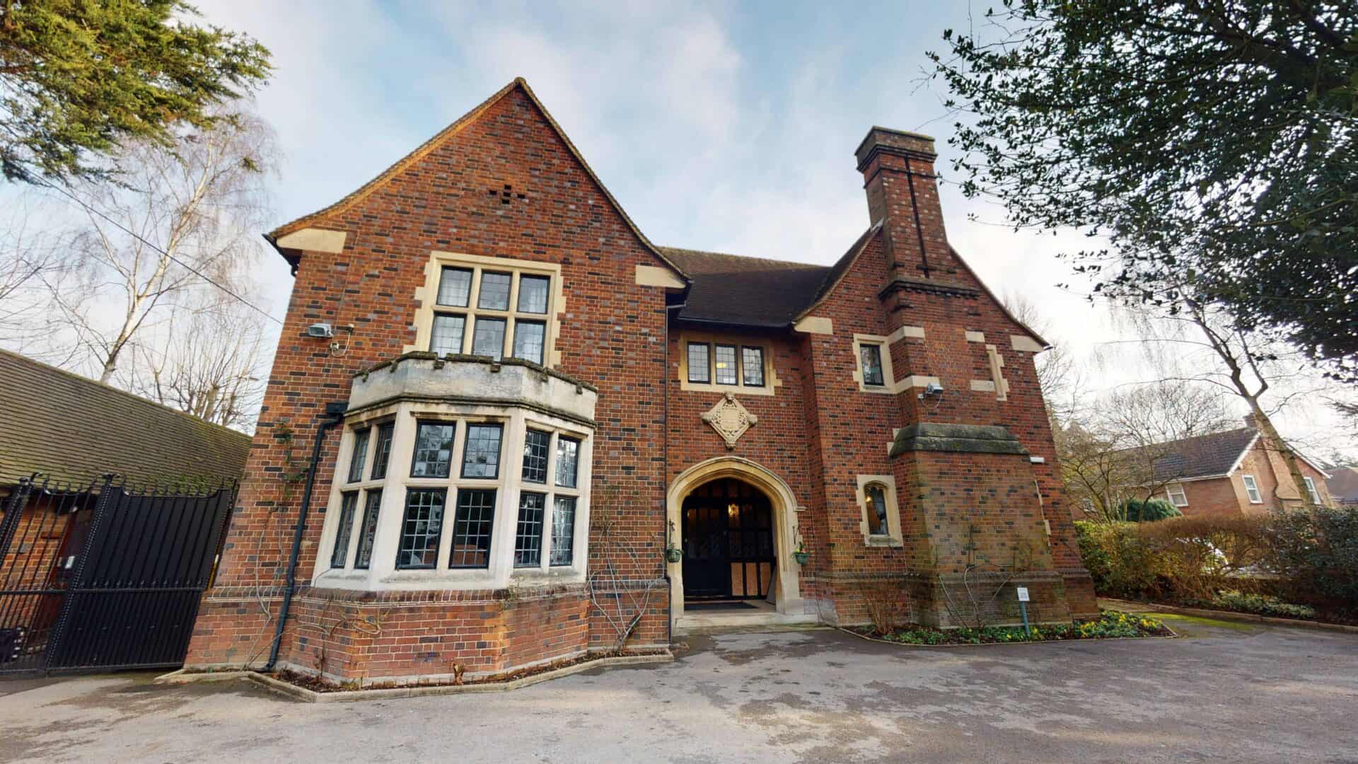 A charming brick house with a bay window and an arched doorway, nestled in a tranquil neighborhood with mature trees, offering respite care for elderly patients.